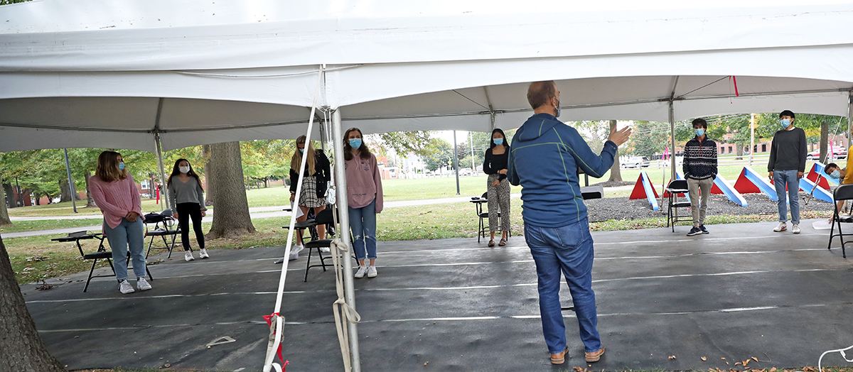 Music Department Chair Kris Johnson conducts rehearsal under a tent.