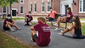 Exeter dorm proctors seated on the ground waiting to welcome students to campus.