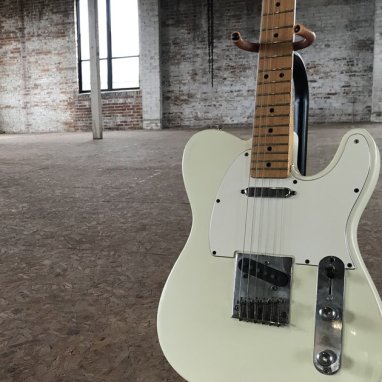 A white electric guitar in an empty room