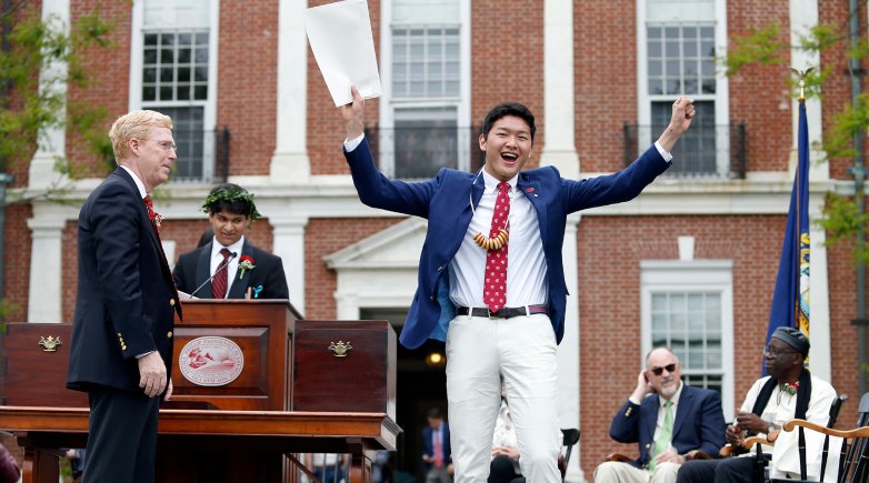 Student raises his diploma in the air with a look of joy at Exeter's Commencement. 
